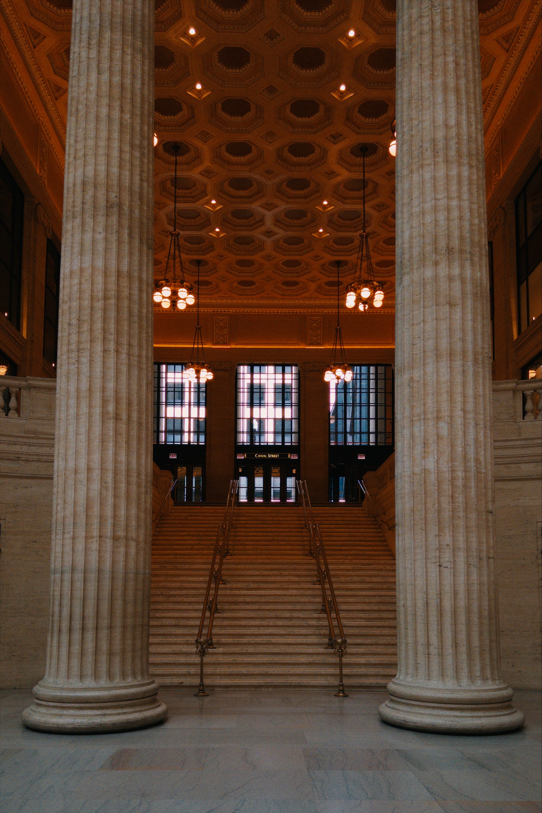 Photo from Union Station in Chicago featuring a big stone staircase with tall windows and an ornate ceiling in the background with two large marble columns on the sides in the foreground. This was featured in the 1987 film The Untouchables.